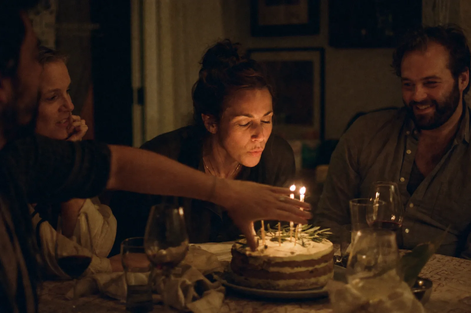 Friends around a homemade birthday cake lit only by its candles