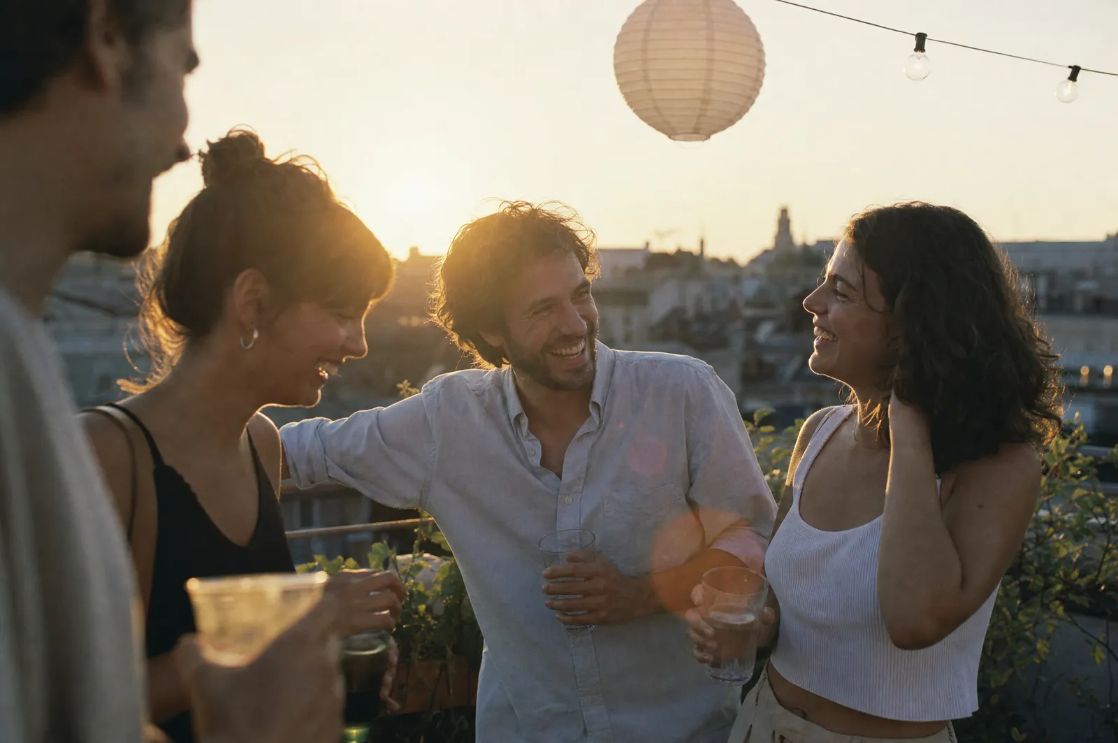 Four friends laughing together at a rooftop party at sunset