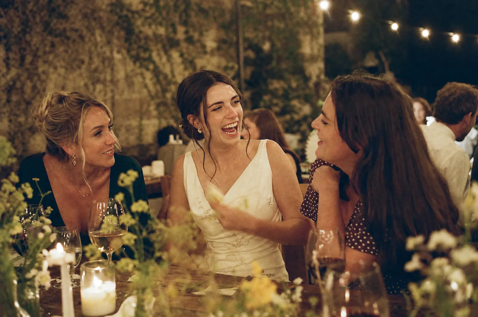 Guests laughing with the bride at a candlelit wedding reception table